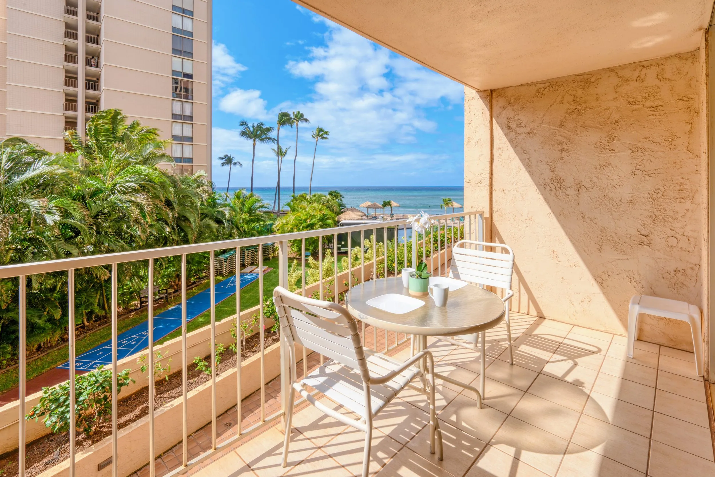 Second-floor lanai with a table and chairs looking out over palms to the ocean